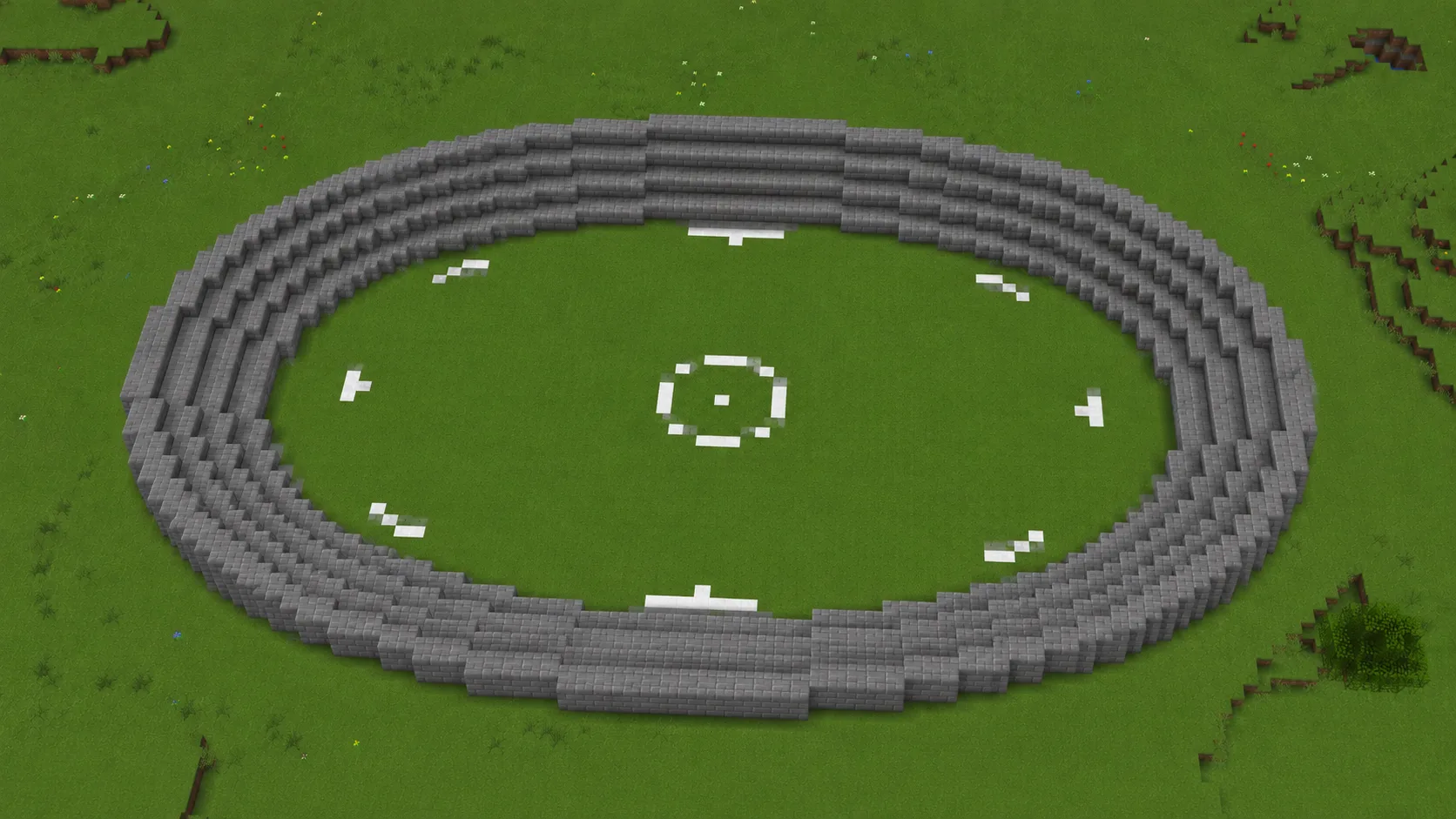 A Minecraft stadium from above, three stepped rings of stone seating around an oval grass field marked with a white centre circle